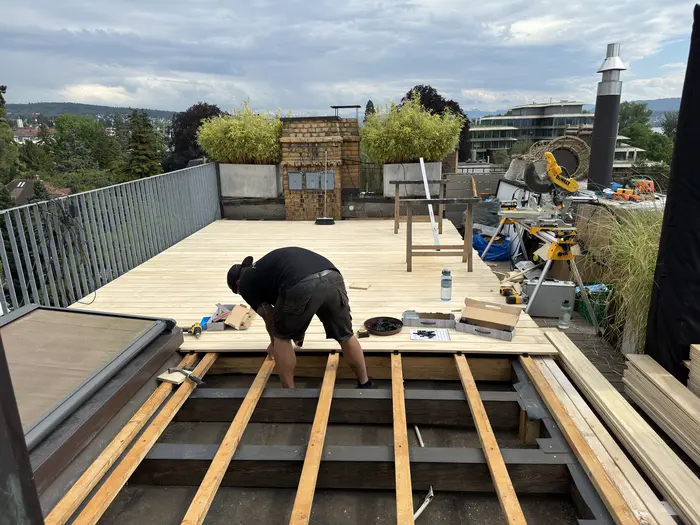 Handwerker verlegt Terrassendielen auf einer Dachterrasse in Zürich